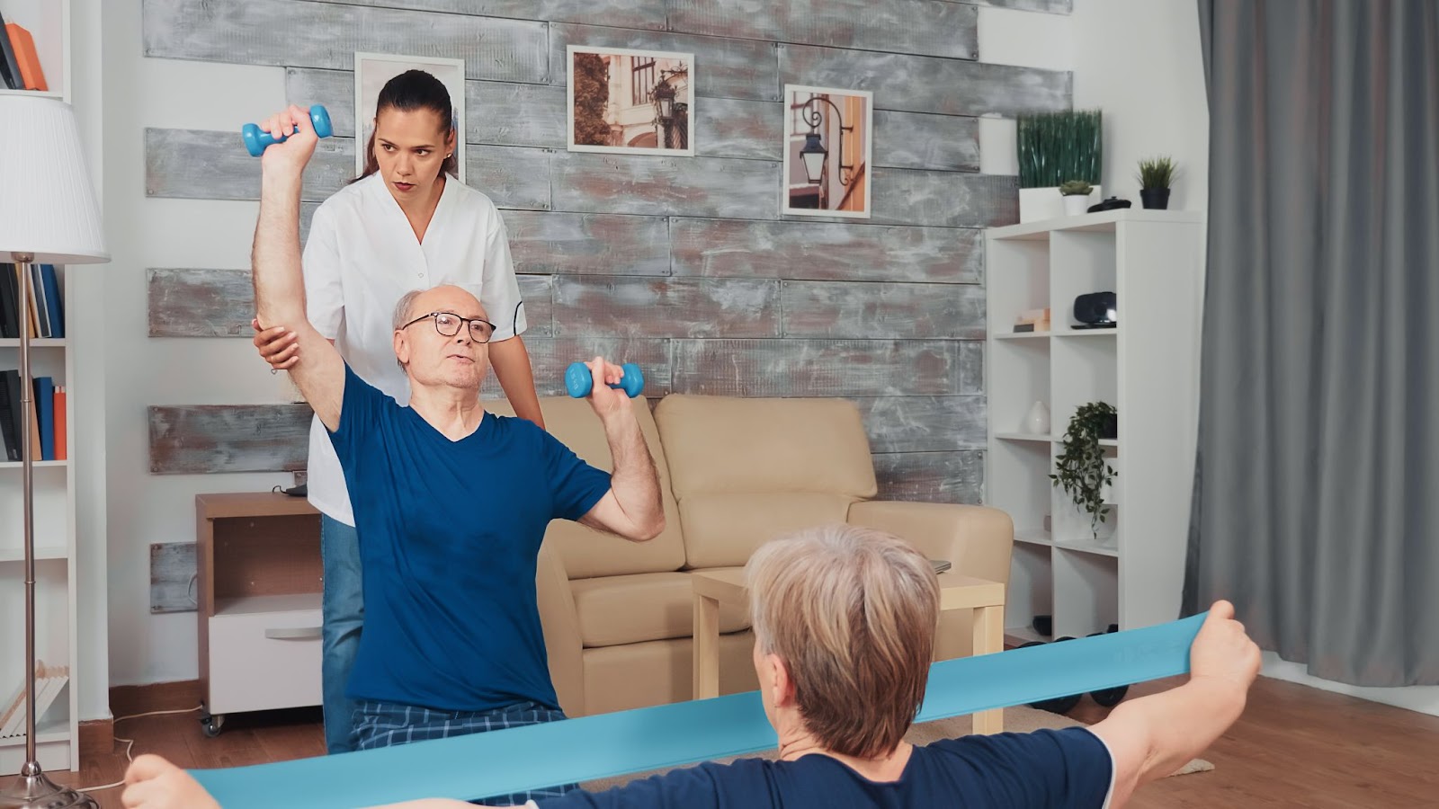 Elderly man doing arm exercises with physiotherapist and an elderly woman using resistance band