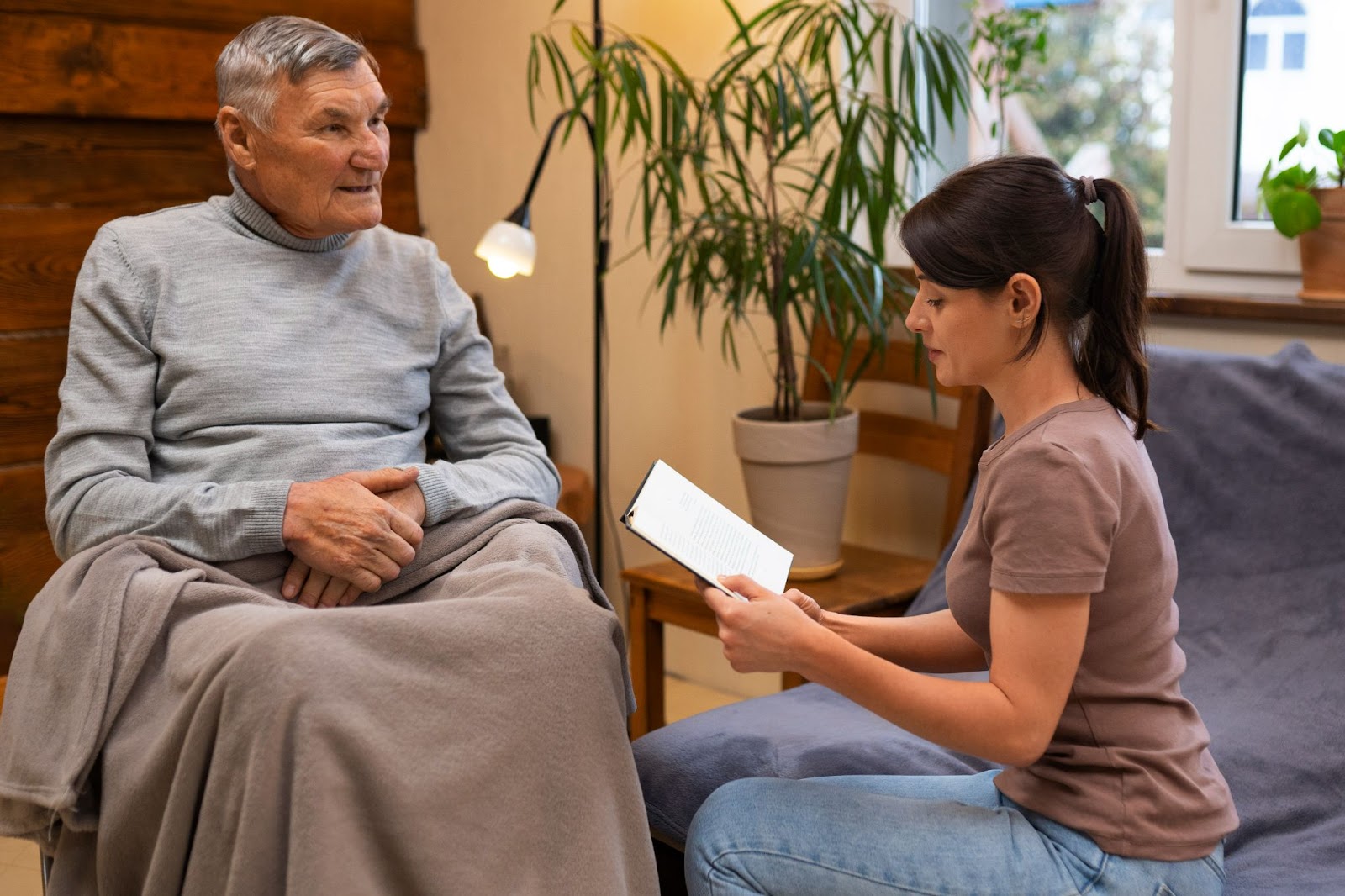 Carer reading to senior man in a comfortable home environment as part of personalised dementia aged care